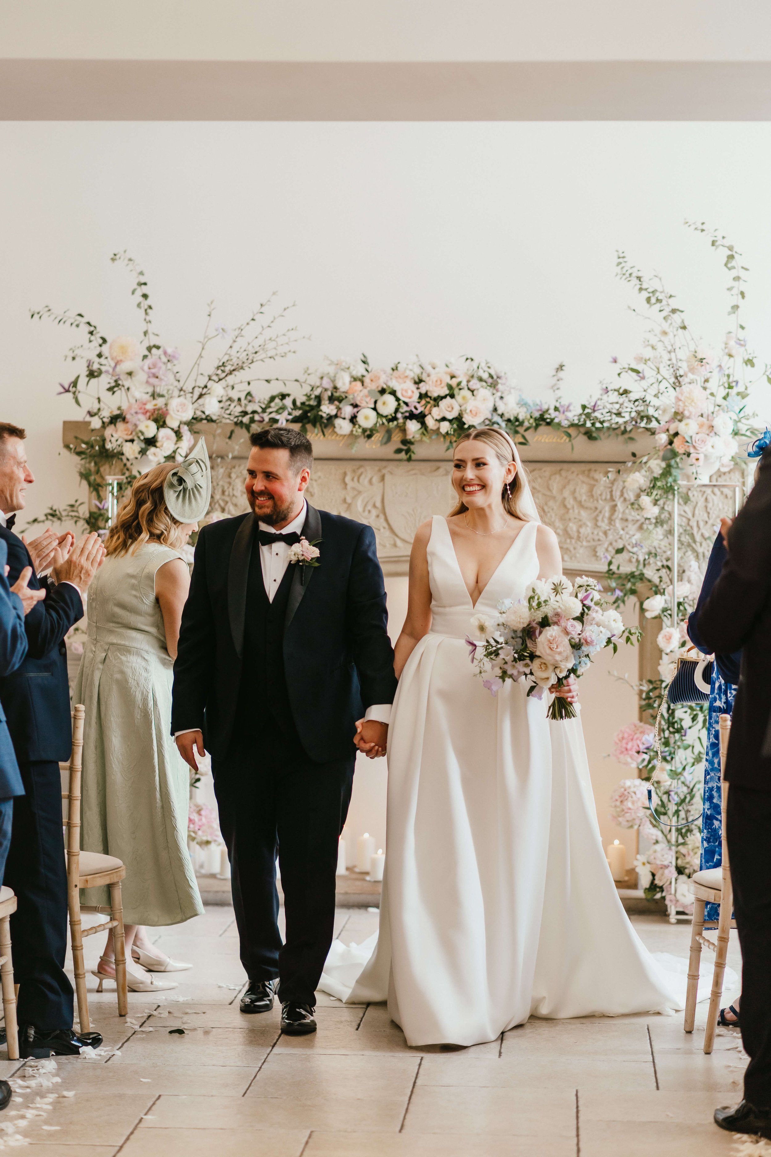 Bride in an elegant white dress with a groom in black tie carrying a luxurious bridal bouquet pastel ceremony flowers in the background at Tyn Dwr Hall wedding venue