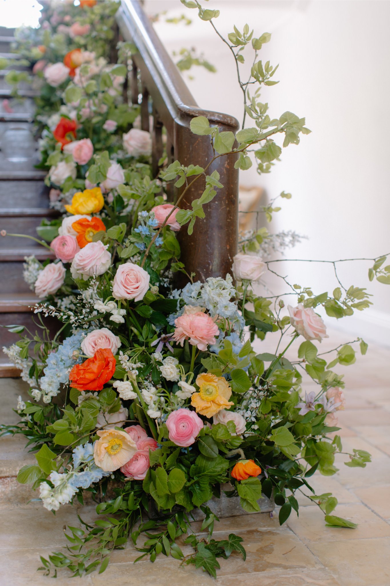 Colorful floral arrangement with pink, yellow, orange, and blue flowers cascading along a rusted metal railing on a staircase.