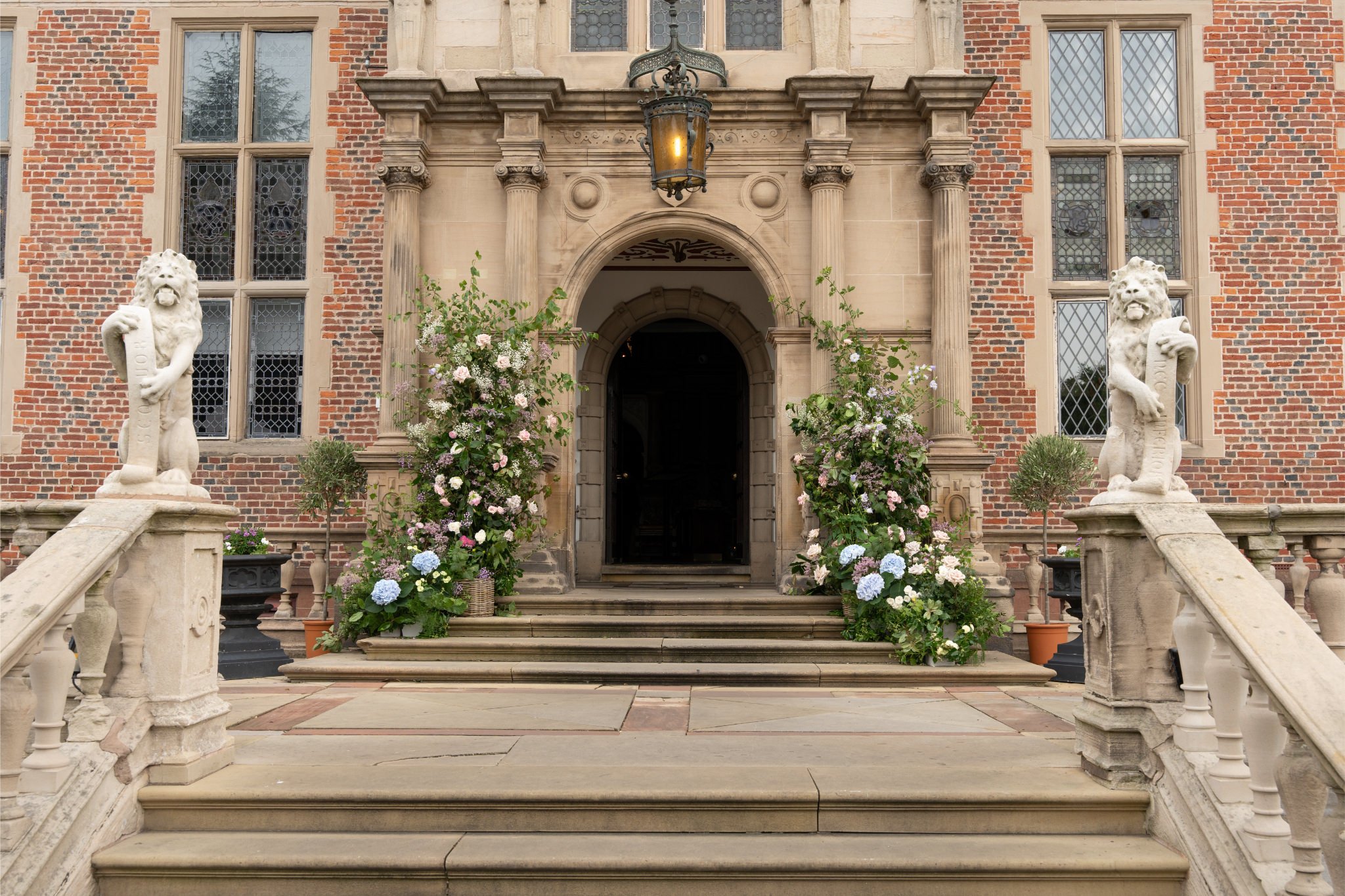 Entrance to a historic building with stone steps, two lion statues, and lush flower arrangements.