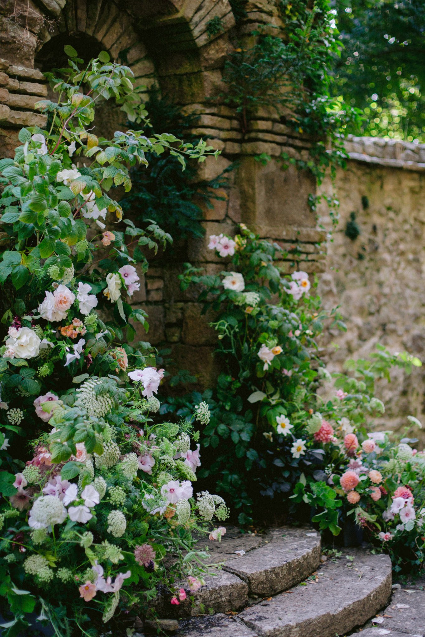 Colorful flowers blooming on a stone steps in front of an old stone wall with green foliage.