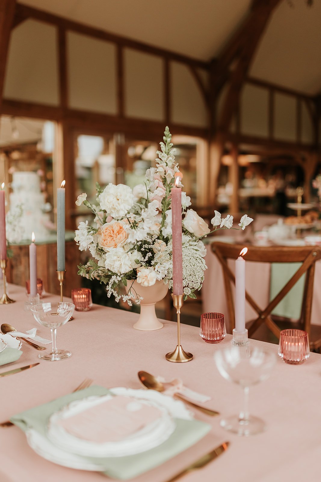 Elegant wedding table centerpiece with pink, white, and peach flowers, surrounded by pink and gray taper candles, and pink glass votives.