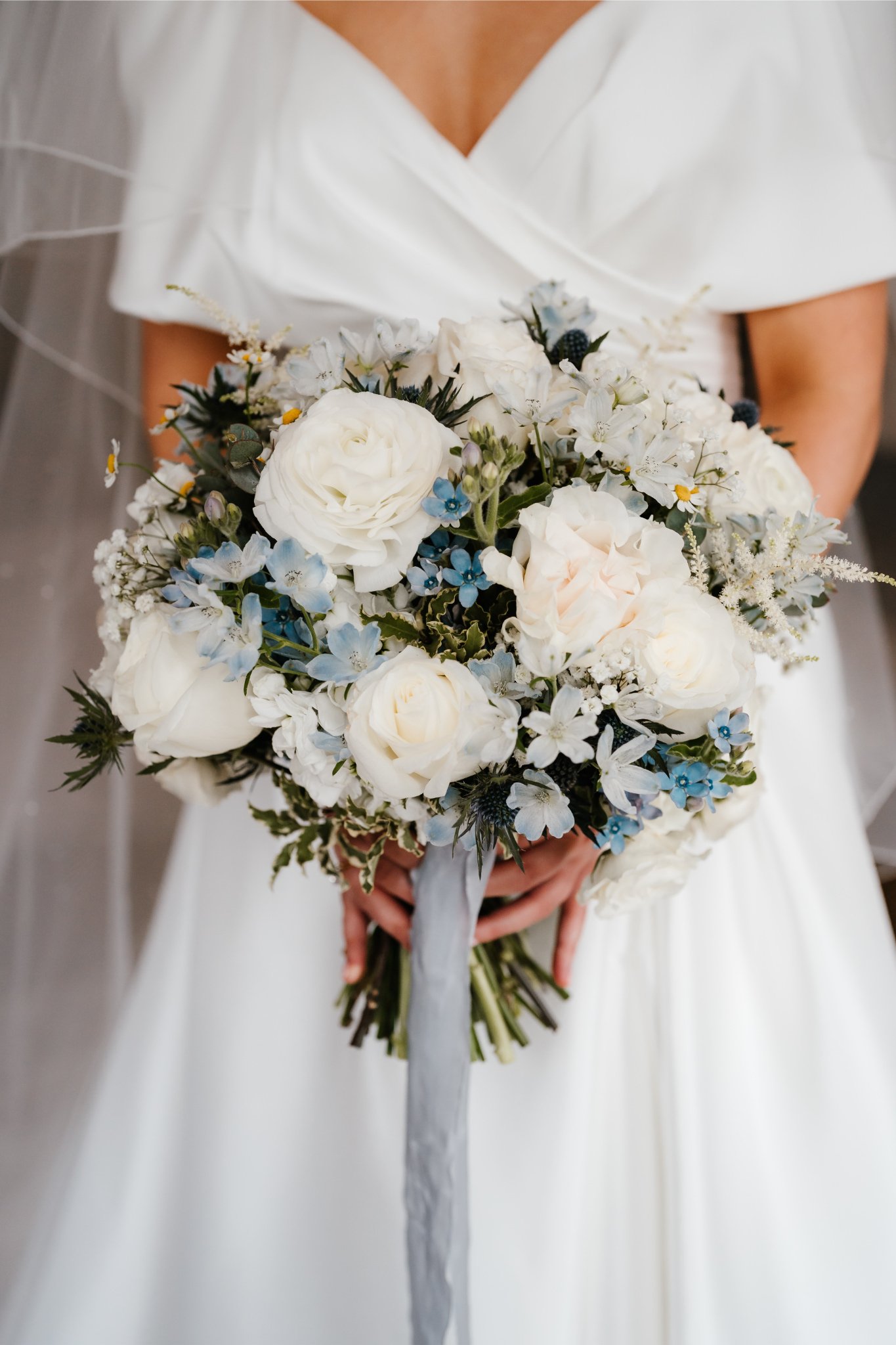 Bride in white dress holding a large bouquet of white and blue flowers.
