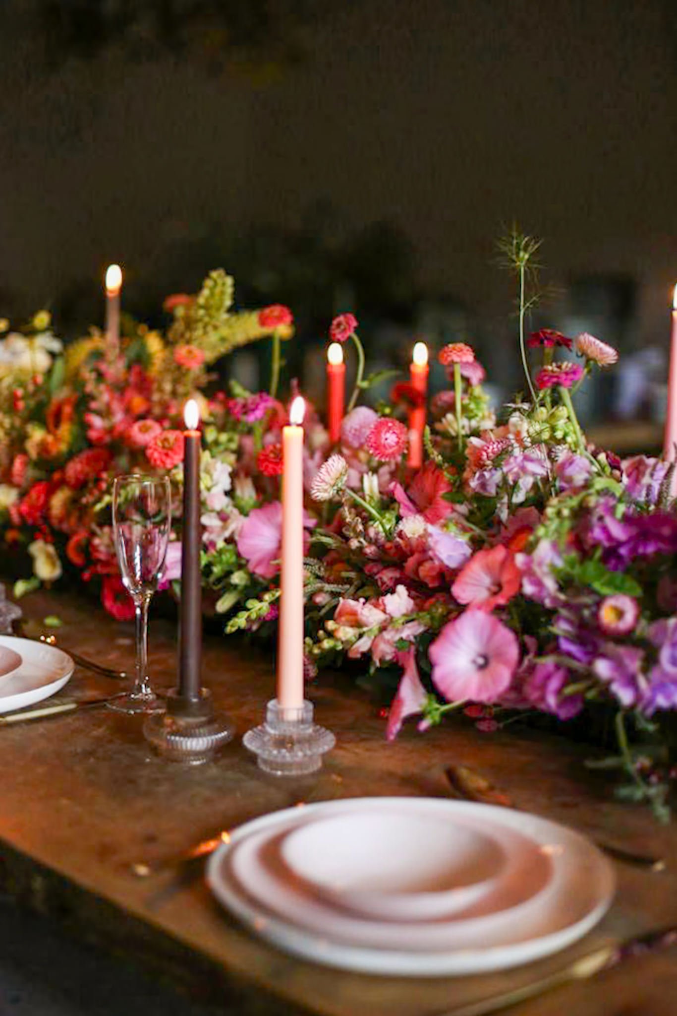 A table decorated with a large, colorful flower arrangement and lit candles, set for a celebration or dinner event.