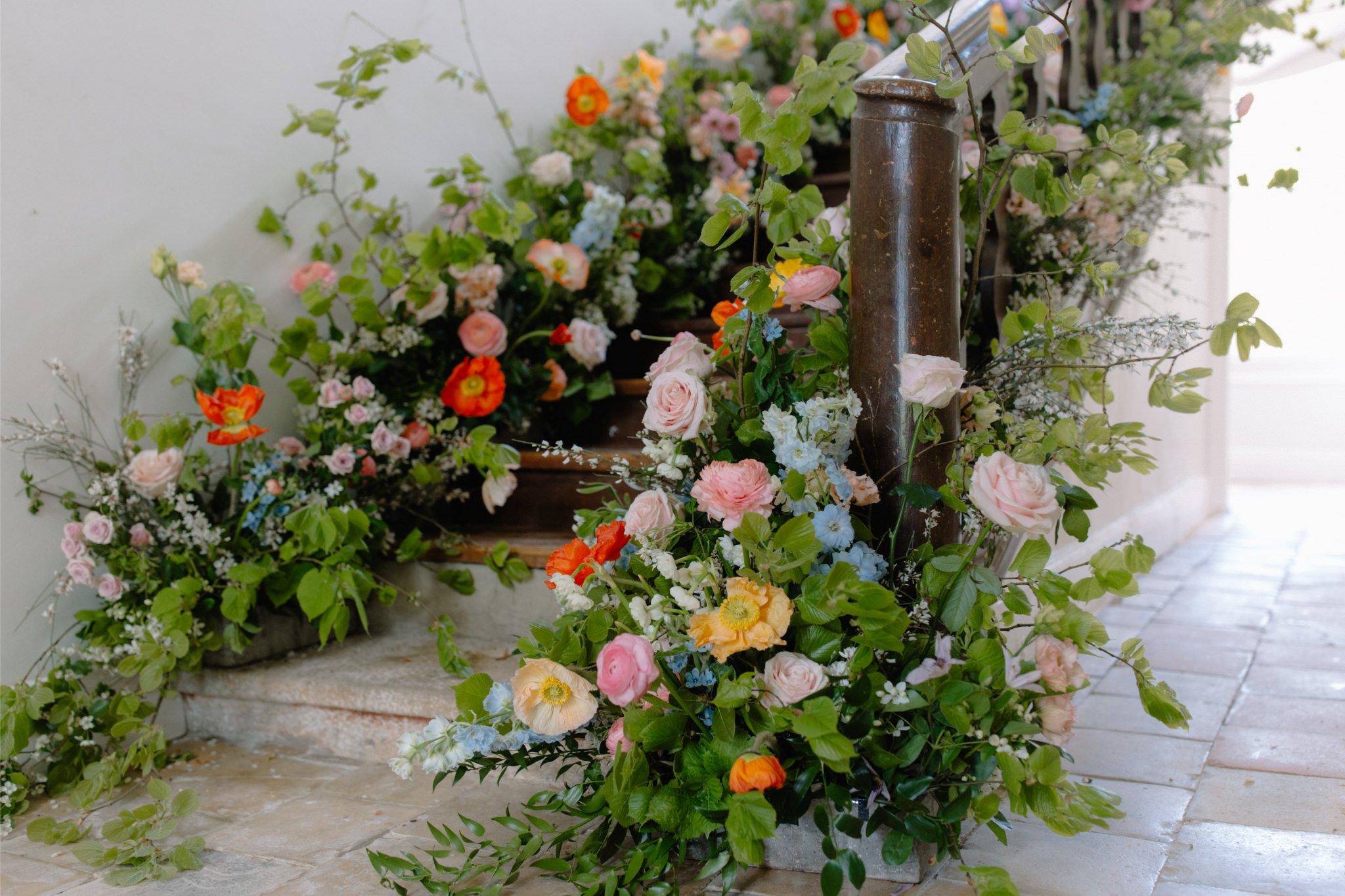 Colorful floral arrangements with roses, poppies, and other flowers around a wooden stand on a brick floor.