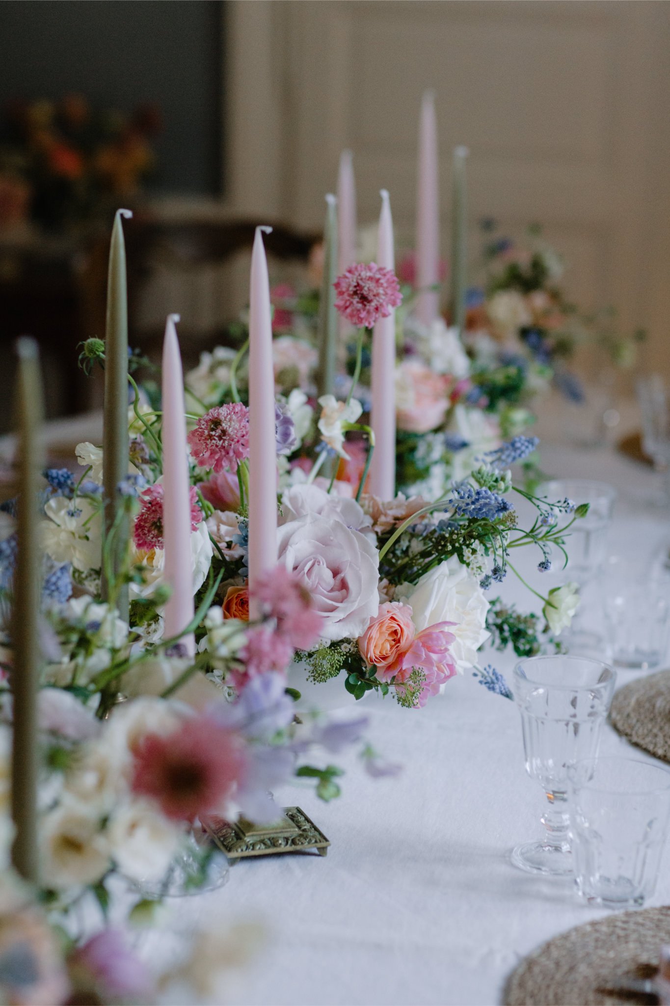 Elegant dining table centerpiece with pink, white, and purple flowers, tall candles, and glassware.