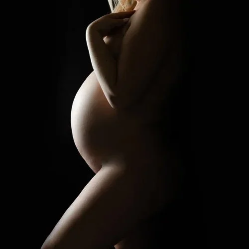 Silhouette of a pregnant woman with her hand resting on her chest, against a dark background.