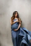 Pregnant woman sitting against a gray wall, wearing a blue dress