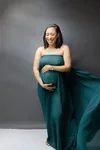 A woman wearing a teal dress, standing against a gray background, holding the fabric of her dress.