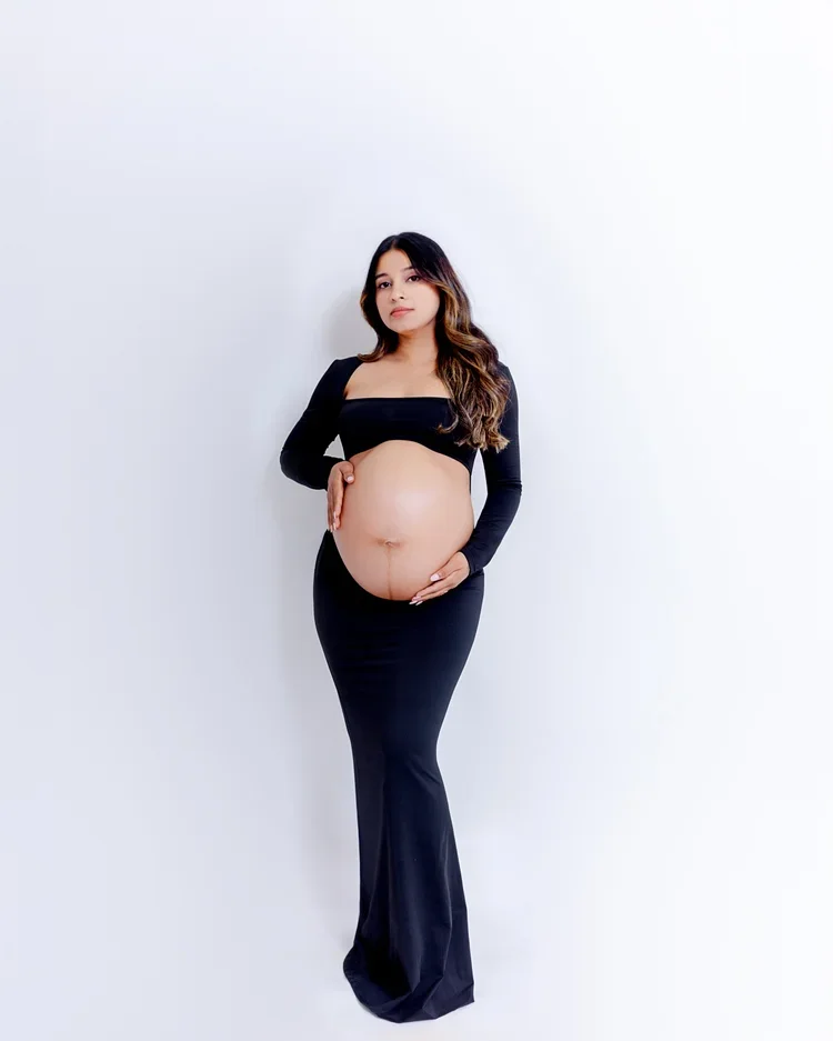 Pregnant woman in a black dress standing against a plain white wall.