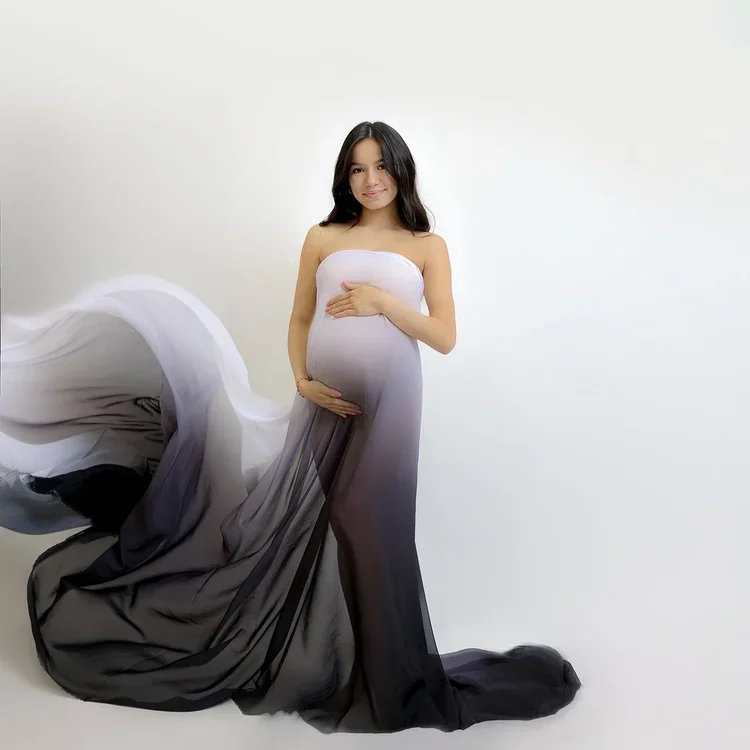 Pregnant woman in a flowing black and white gradient gown against a plain white background.