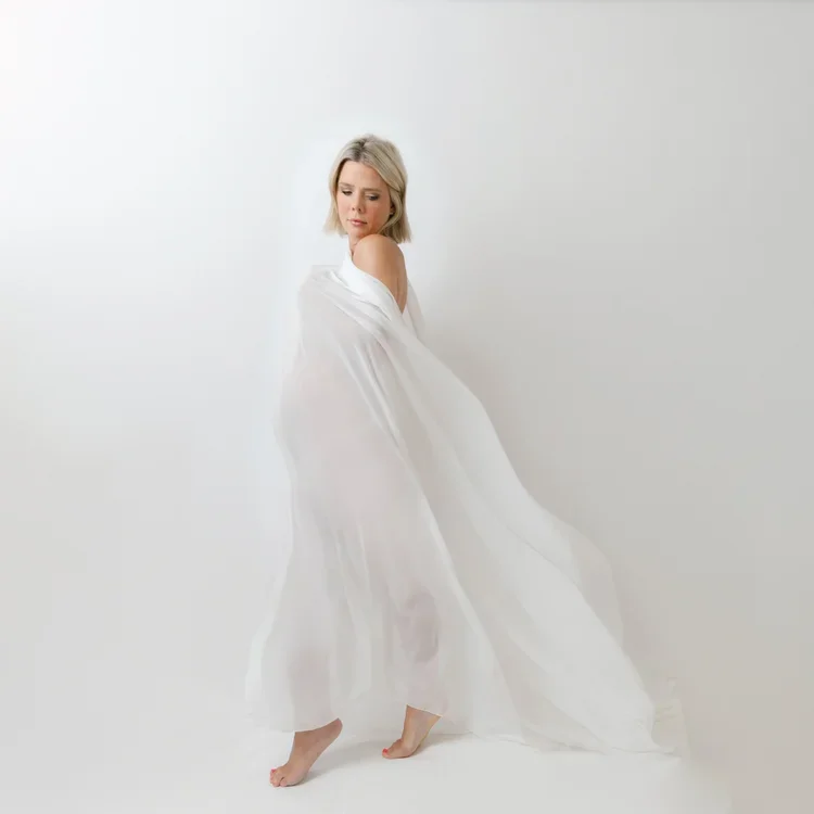 A woman with blonde hair in a white dress standing against a plain white background.