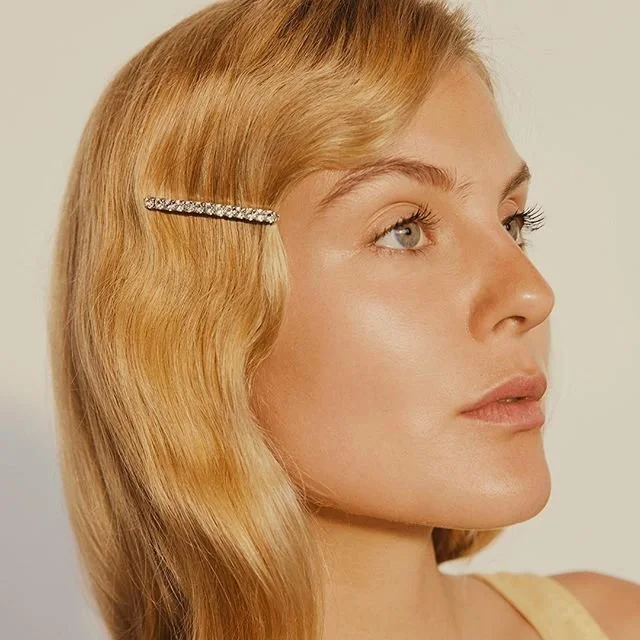 Side profile of a woman with wavy blonde hair and a rhinestone hair clip.