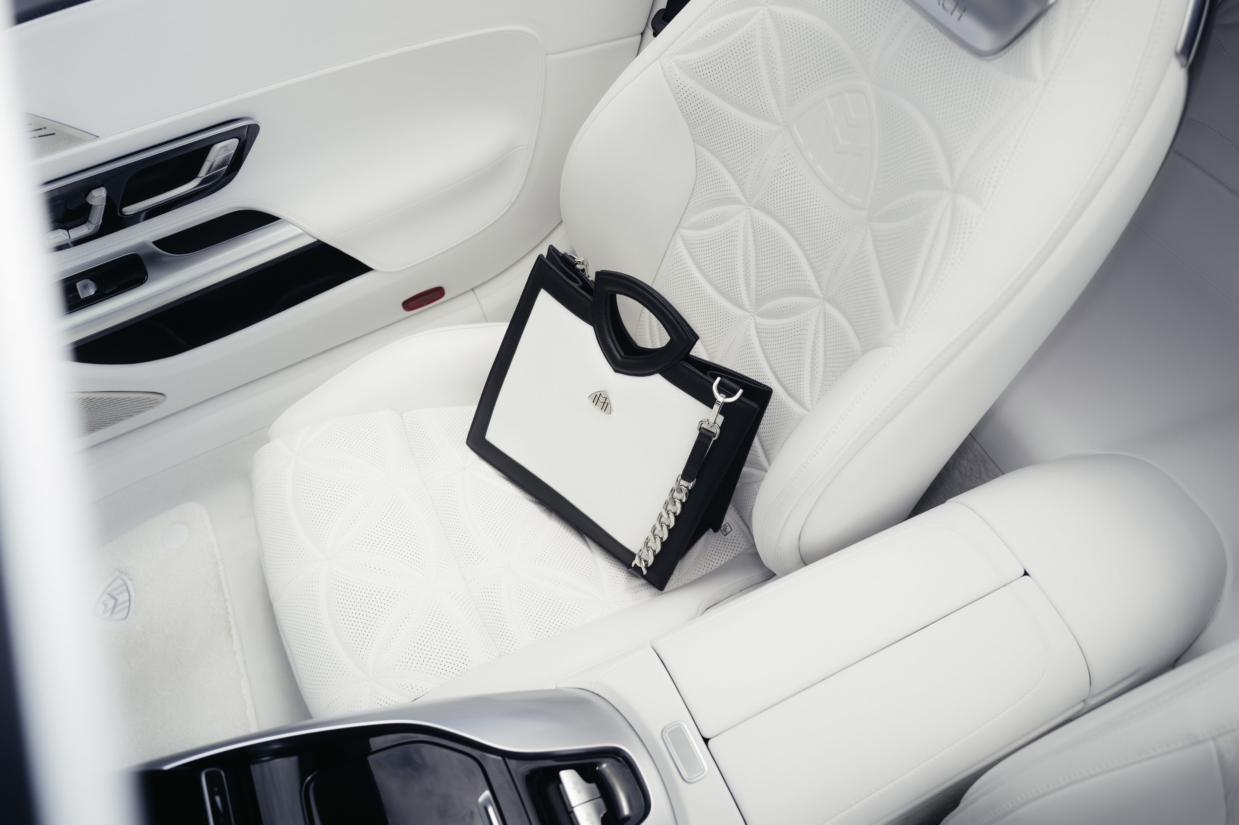 Interior of a luxury car with white leather seats and a black and white handbag on the passenger seat.