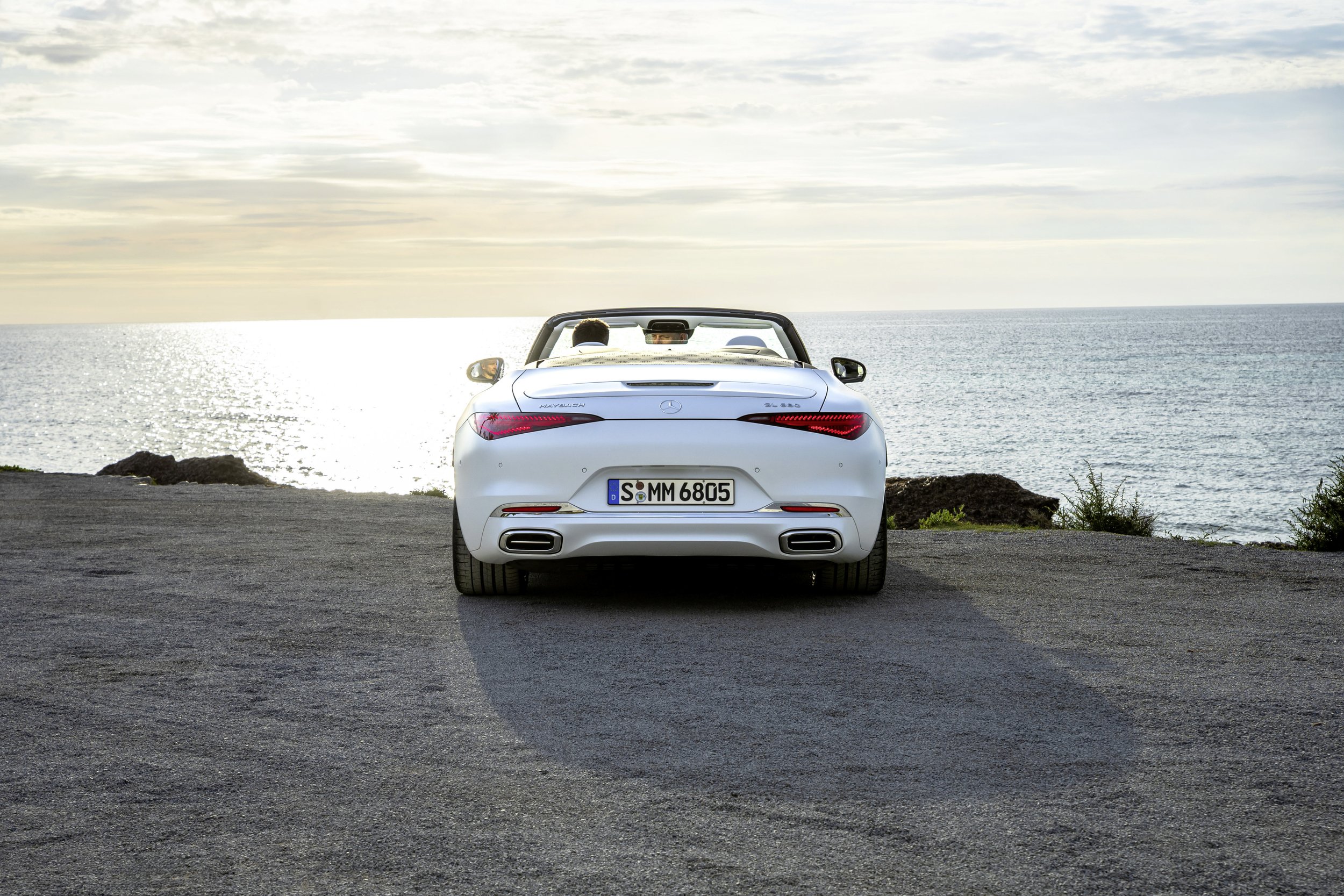 White convertible Mercedes-Benz car parked on pavement facing the ocean at sunset.