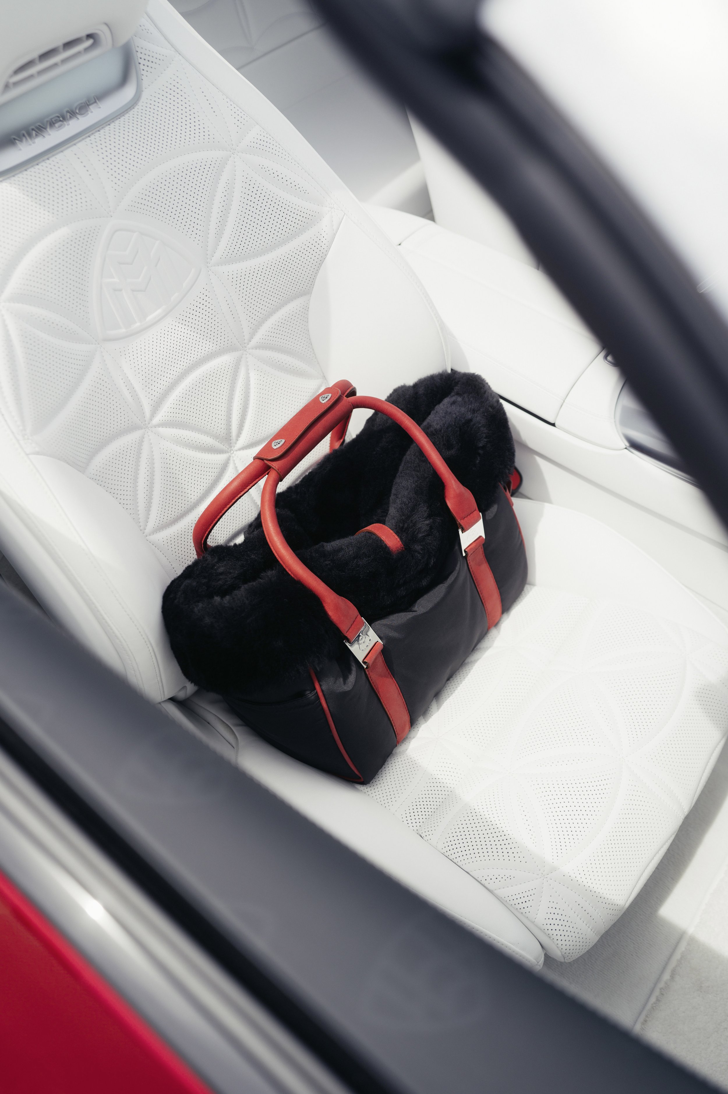 A black and red duffel bag with a fur-lined opening sits on the white leather seat of a car.