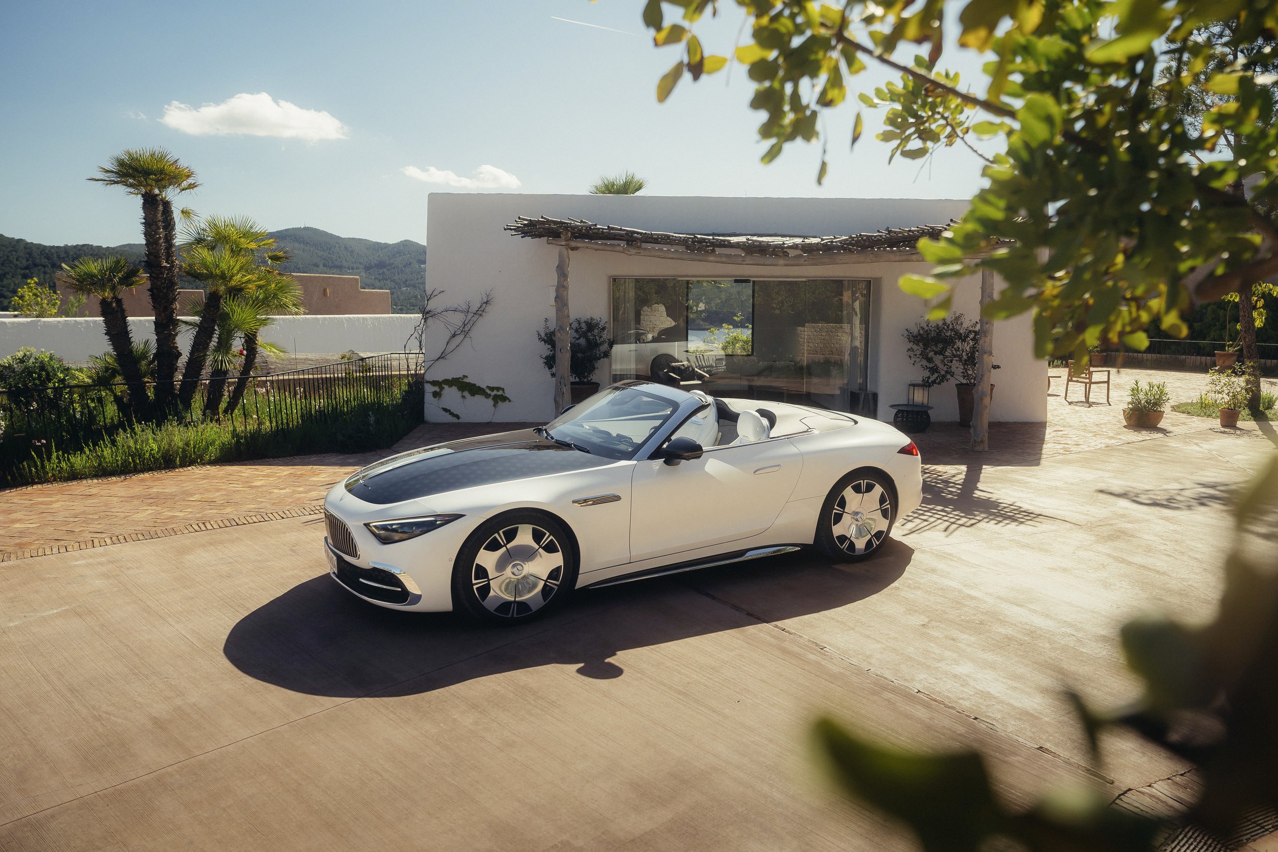 A white convertible luxury car parked in front of a modern white house with a patio and lush greenery.