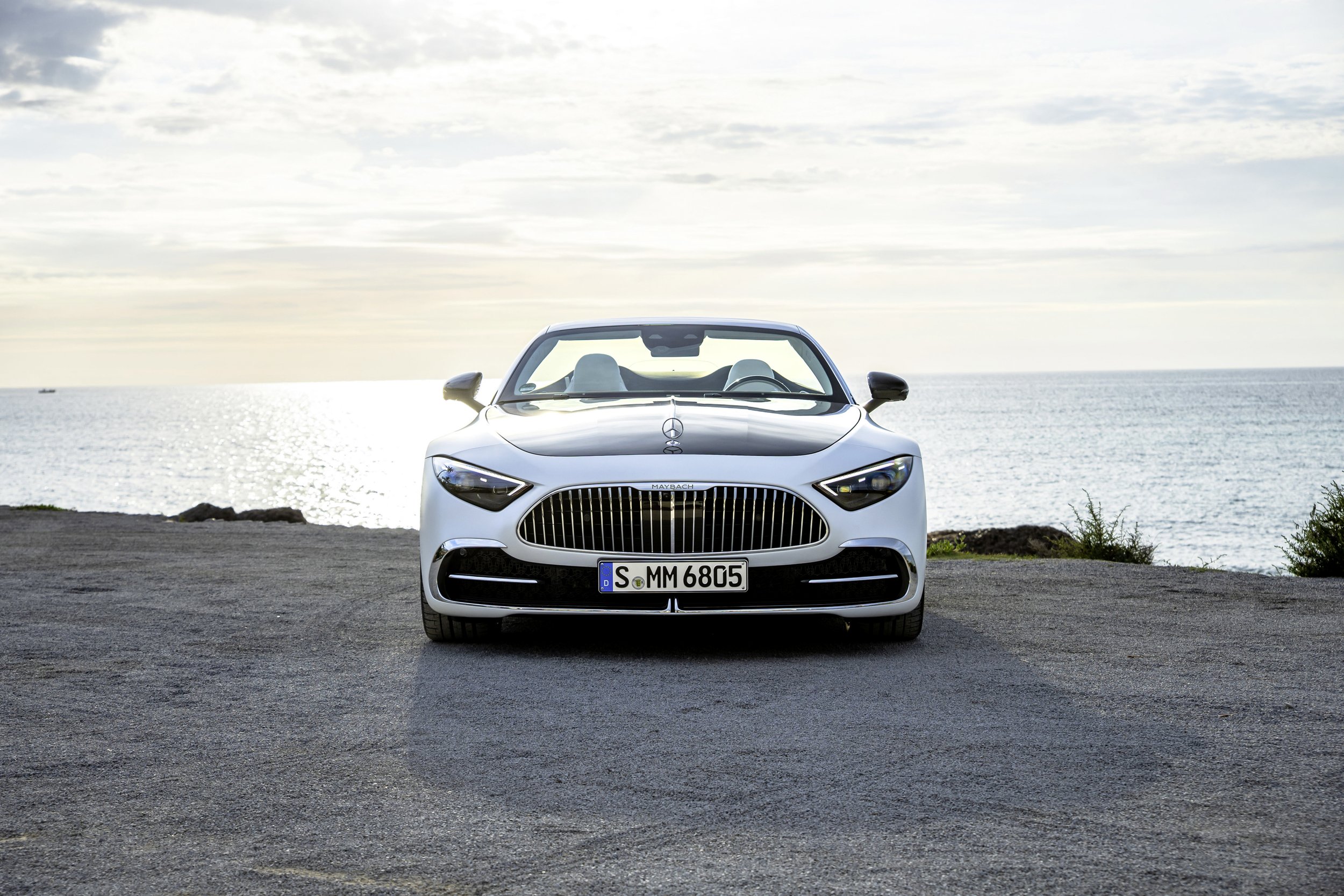 A white luxury convertible car parked on pavement near the ocean, with the sea and sky in the background.