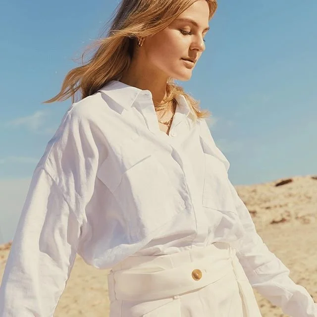Woman in white blouse and high-waisted trousers on a sunny beach