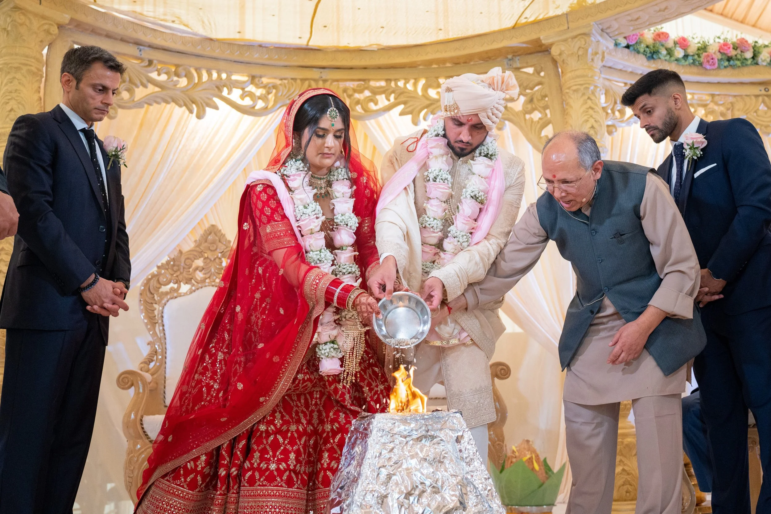 Indian wedding ceremony with bride and groom performing a ritual, surrounded by guests, in a decorated venue.