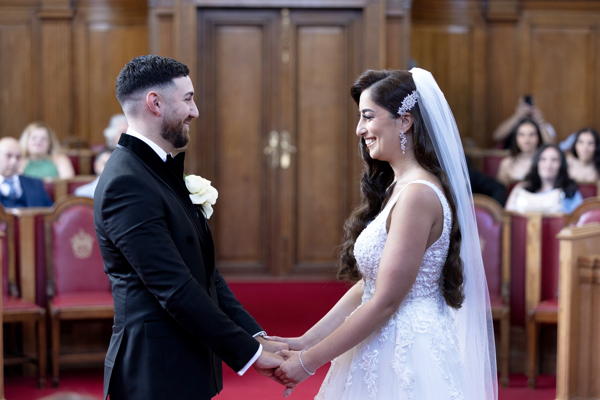 A bride and groom holding hands during their wedding ceremony inside a church with wood-paneled walls and seated guests observing.