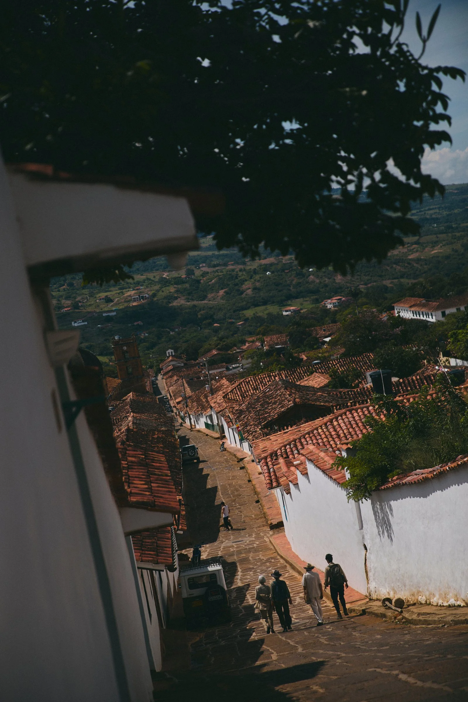 View from Casa Barichara down a steep stone street lined with whitewashed houses and red-tiled roofs in Barichara, Colombia.