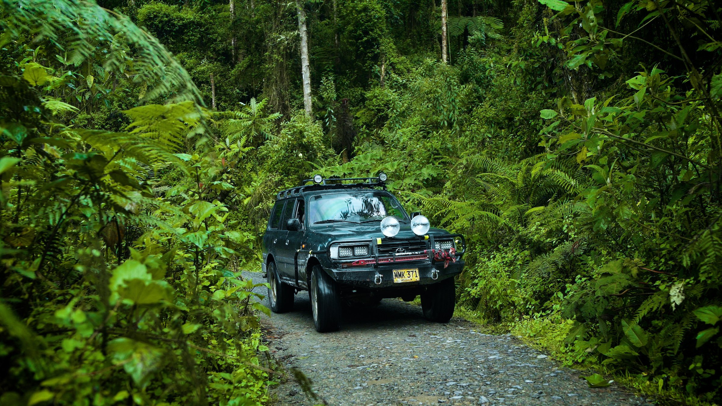 A four-wheel-drive vehicle carrying travelers along a narrow forest road in remote Antioquia, Colombia.