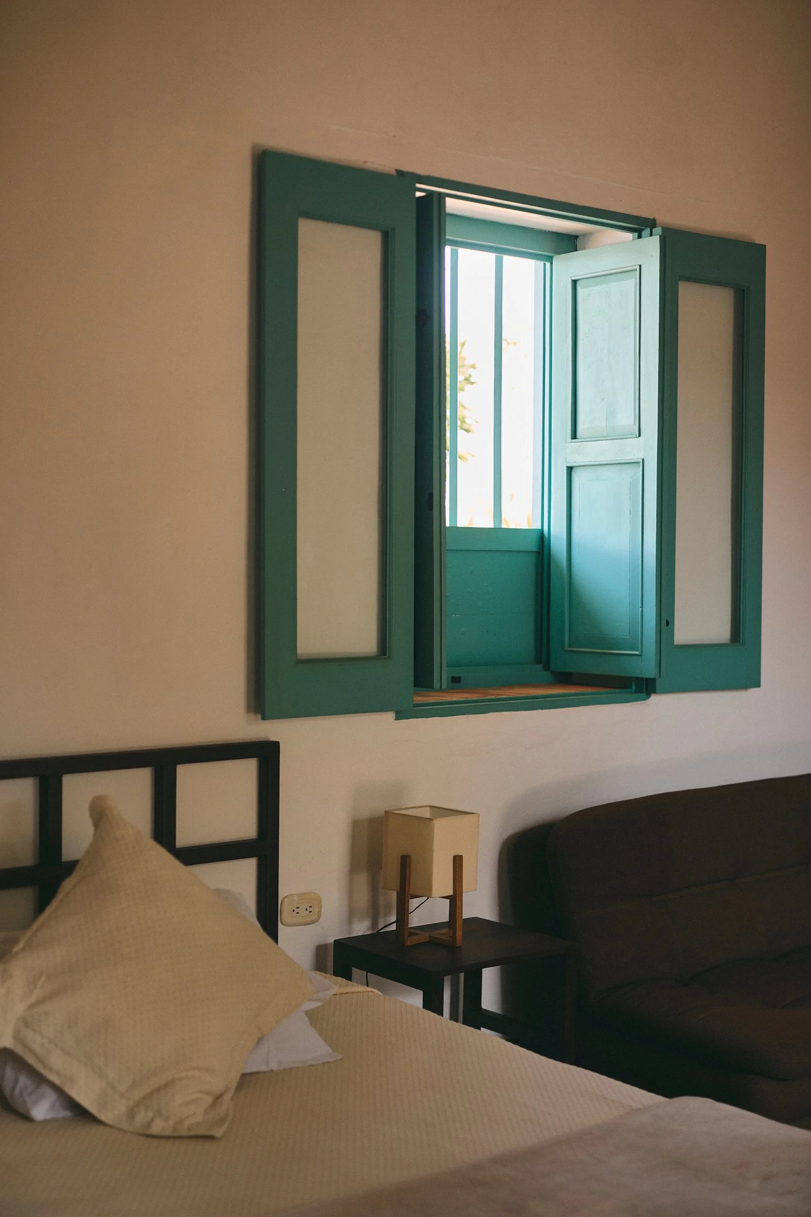 Guest room at Casa Barichara with a turquoise wooden window, white walls, bed, side table, and sofa in Barichara, Colombia.