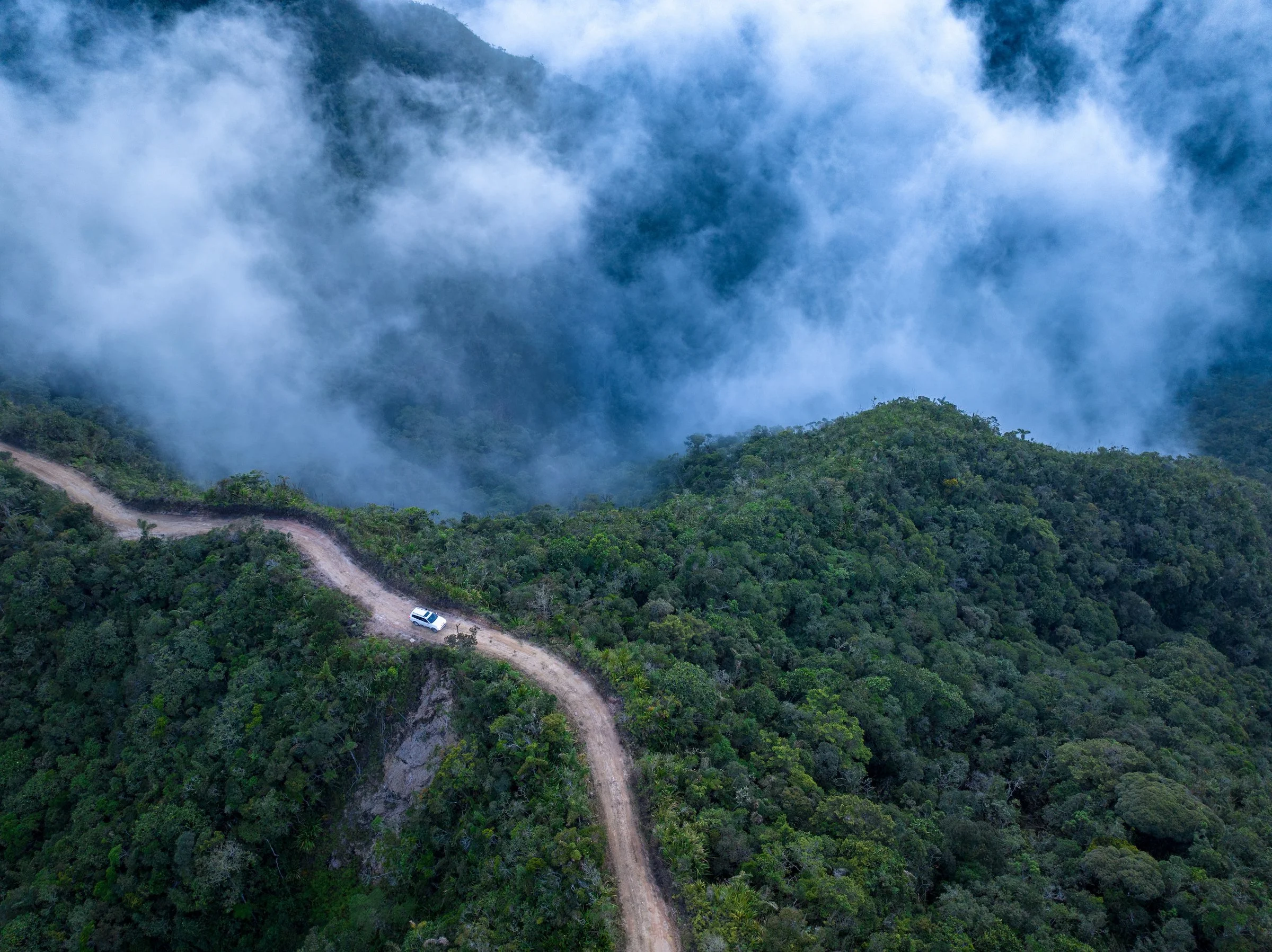 A vehicle travels along an isolated mountain road through forested terrain in Antioquia, Colombia.