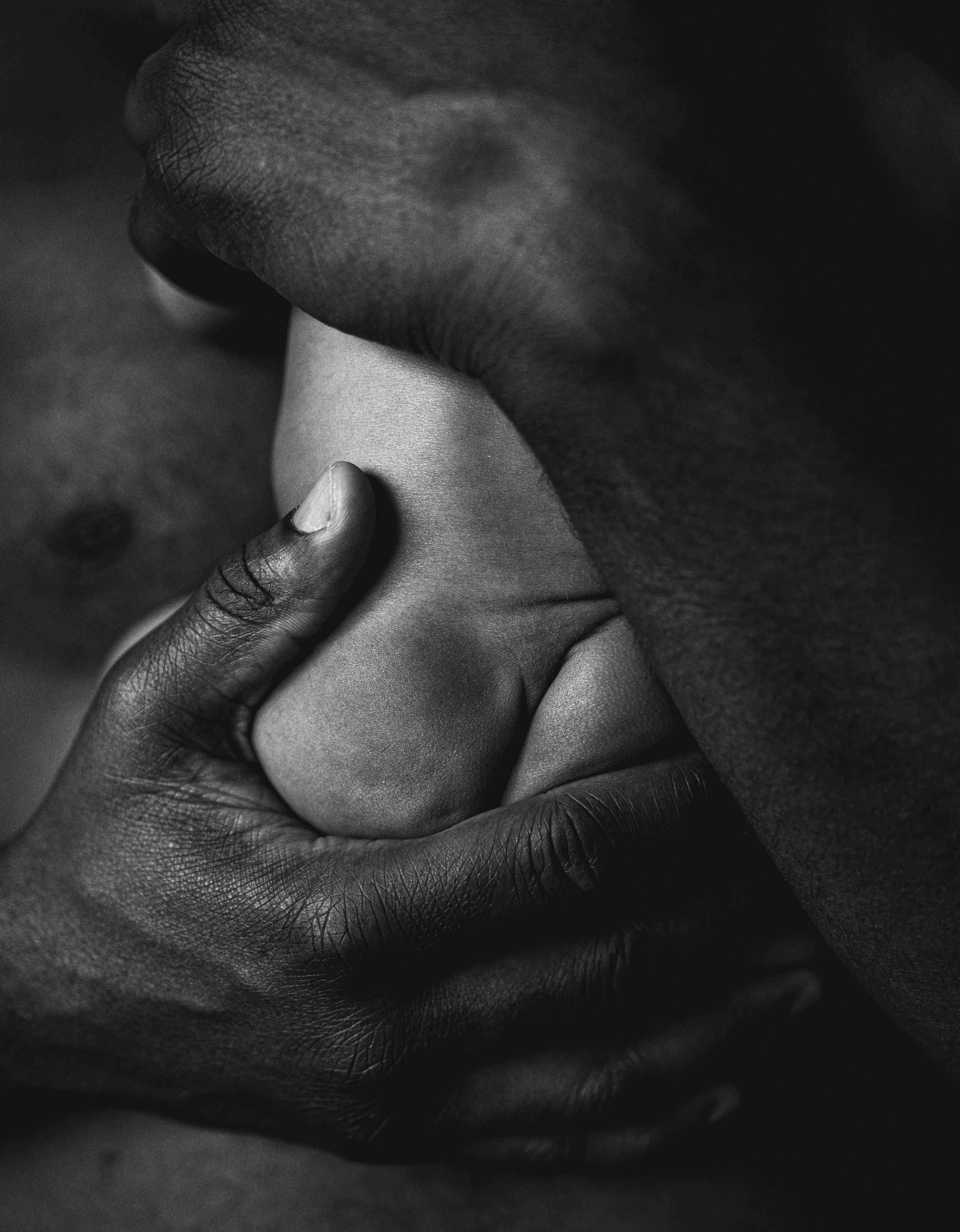 Close-up black and white photo of a person with dark skin holding a light-skinned person's hand.