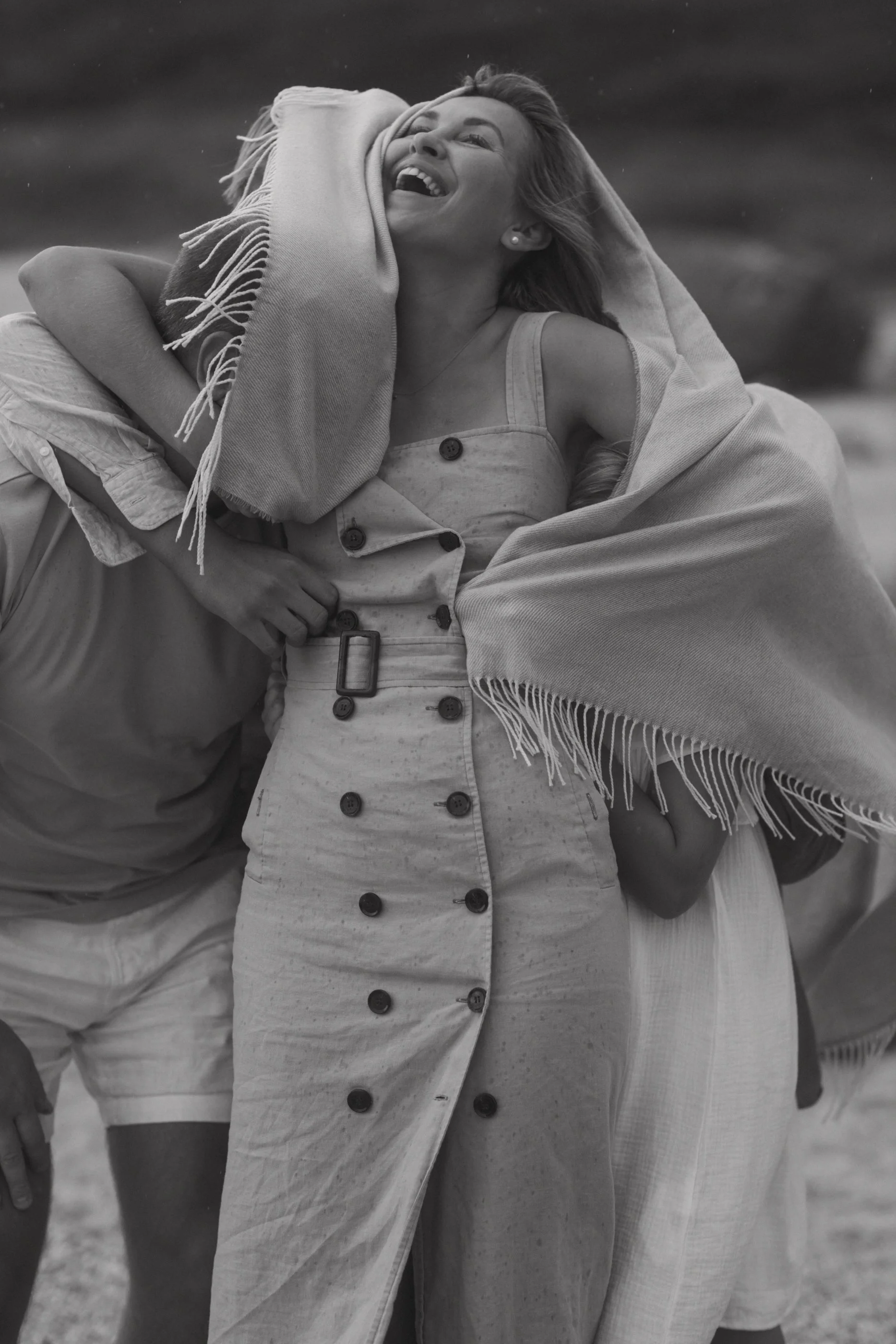 Anastasia Prodous smiling and laughing, wrapping an arm around a person, holding a scarf or blanket over her head with a happy expression, outdoors.