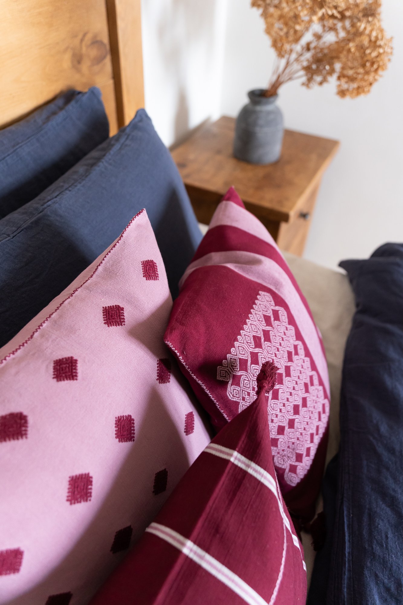 Lifestyle: Stripe Burgundy Cushion with Handstitch Detail, Styled on Bed with Complementary Pale Pink Cushion, Crafted by Indigenous Artisans in Mexico, UN Collaboration - Routes Interiors