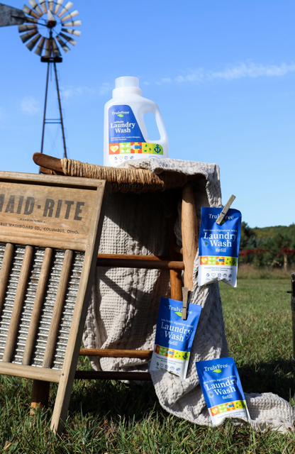 Truly Free Home Laundry Wash Jug and refills sitting and hanging from a table outside in a farm setting