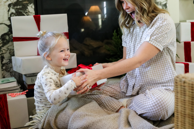 A sitting blonde woman handing a blonde child a holiday gift