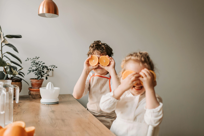 Two kids in white long sleeve shirts holding up orange halves in front of their eyes