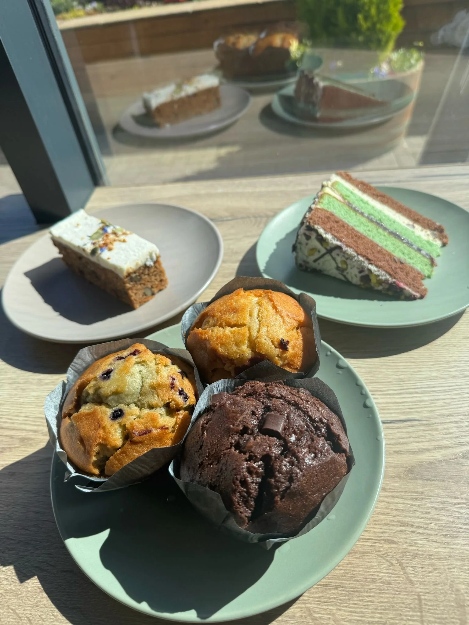 Assorted baked goods on plates, including muffins, layered cake slices, and a fruit cake.
