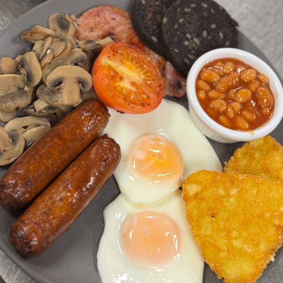 A traditional English breakfast with mushrooms, sausages, a grilled tomato, baked beans, black pudding, hash browns, eggs, and bacon.