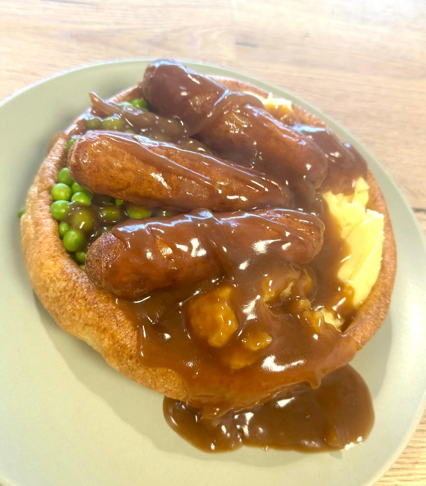 Chopped meatloaf with brown gravy, green peas, and mashed potatoes on a green plate.