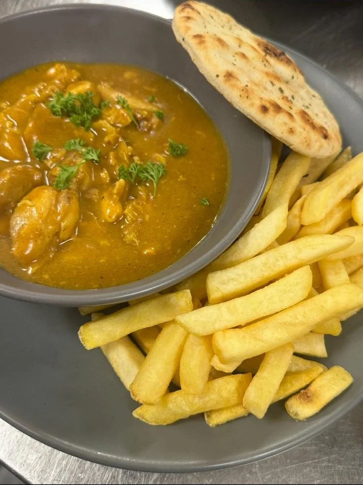 A plate of curry with green herbs, a piece of naan bread, and French fries