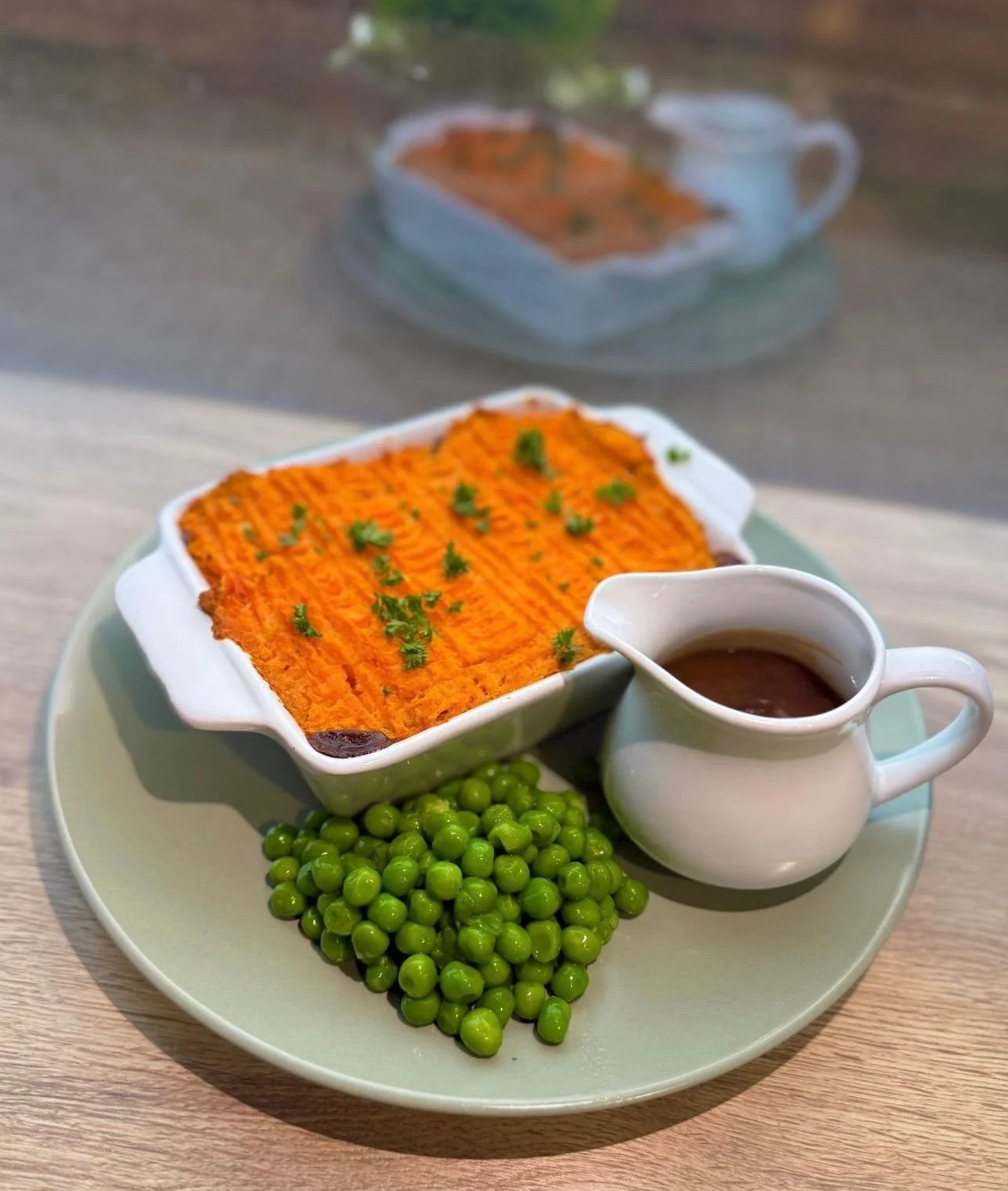 Baked sweet potato casserole garnished with herbs, served with green peas, a small gravy boat of brown gravy, and a cup of cranberry sauce on a pale green plate.