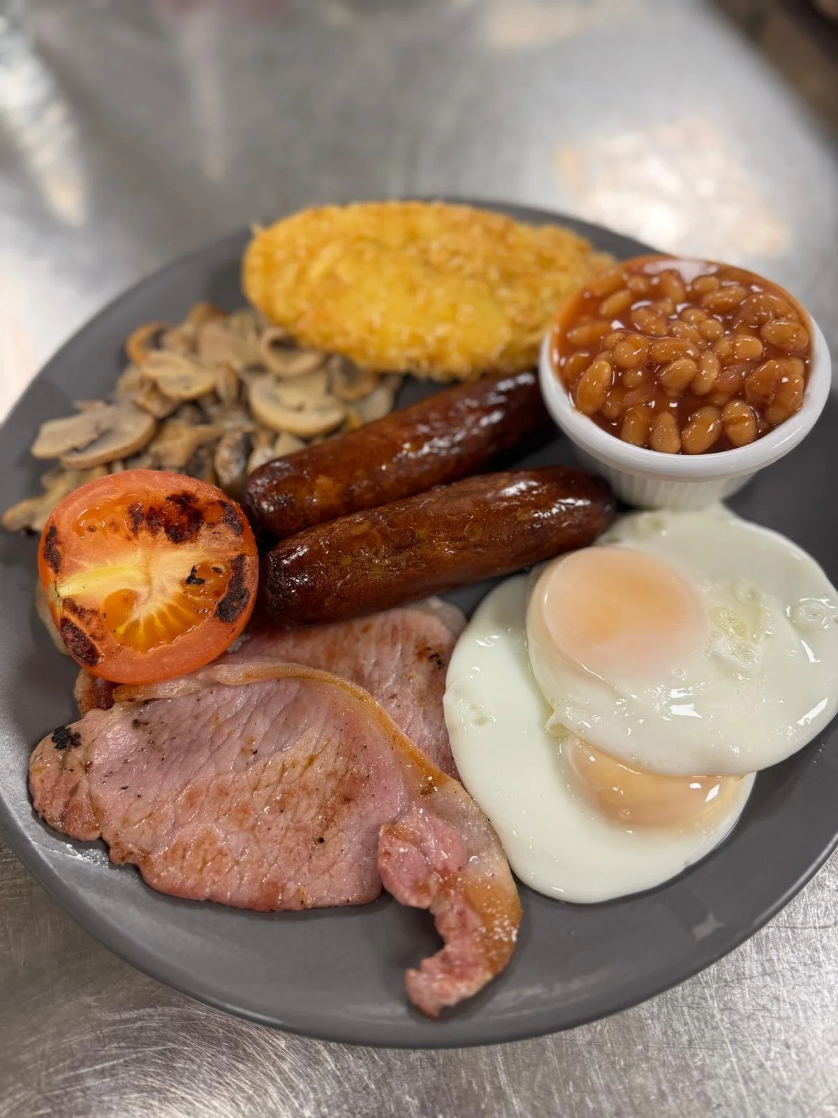 Traditional English breakfast with fried eggs, bacon, sausages, grilled tomato, mushrooms, baked beans, hash brown, and toast