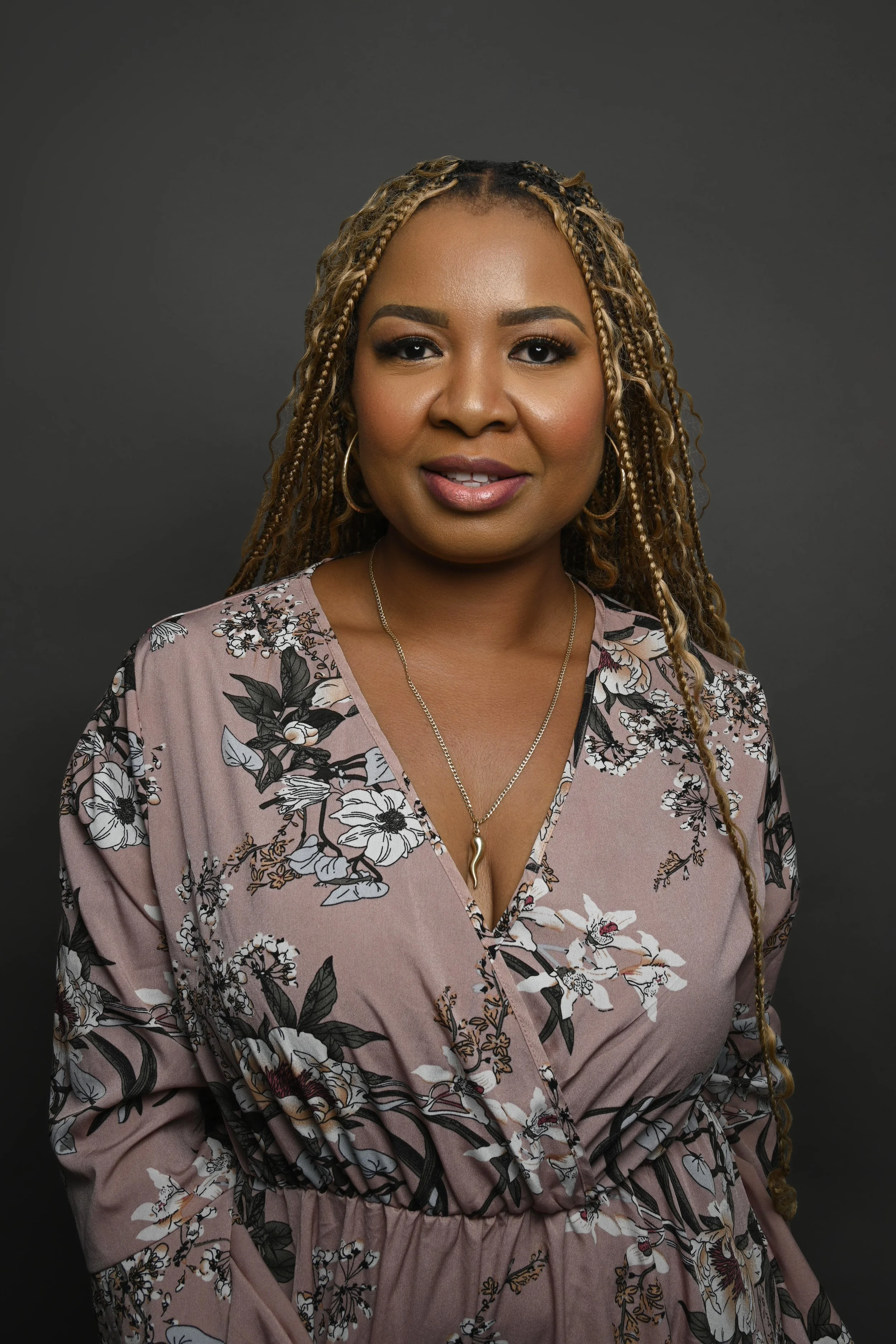 Professional headshot of a woman with long blonde braids wearing a mauve floral dress and gold jewelry, photographed by Whitby portrait photographer