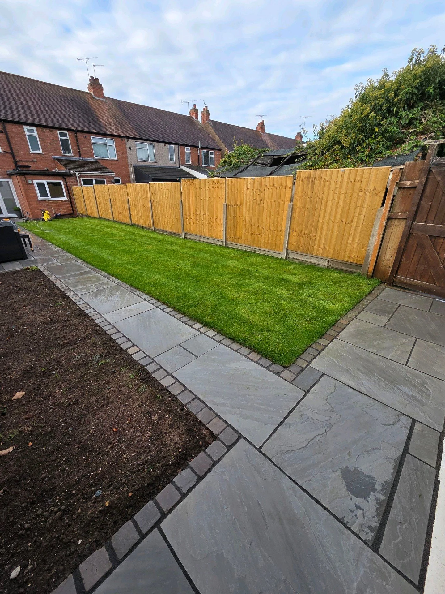 A project we landscaped late last summer for a client in Coventry. 

Tasked with adding a path to the garage, a seating area and a usable lawn we installed an oak sleeper step to split the levels before laying 42sqm of indian sandstone in Kandla grey