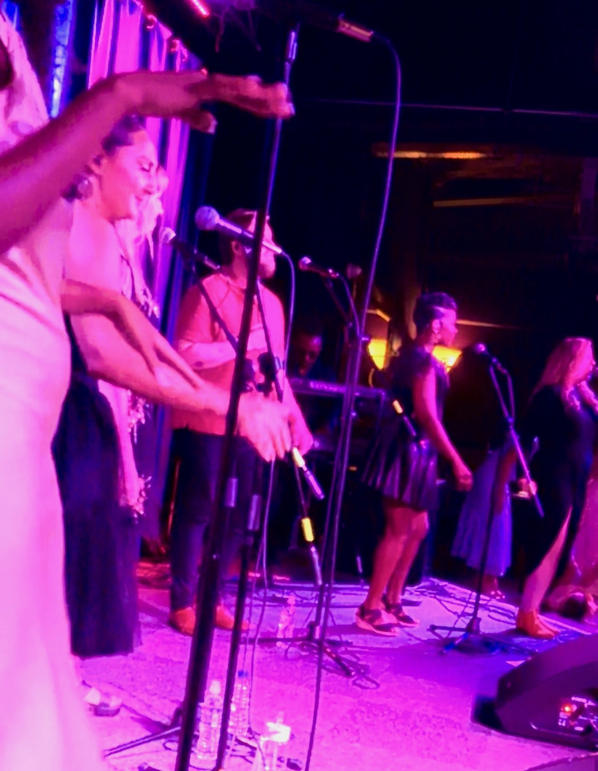 The Tempo Collective singing on stage with microphones, under purple and pink stage lighting.