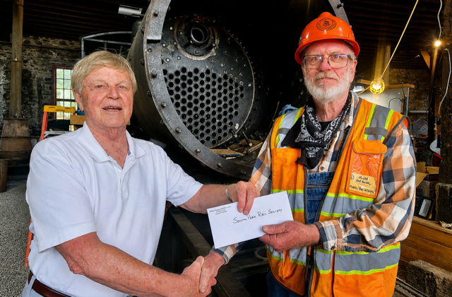 On July 18, 2026, Intermountain Chapter President, Robert Brewster, hands over a Chapter P-R-O Fund check to Paul Blanchard, chief volunteer coordinator at the South Park Rail Society’s newly acquired Como Roundhouse. The check is to be used as match