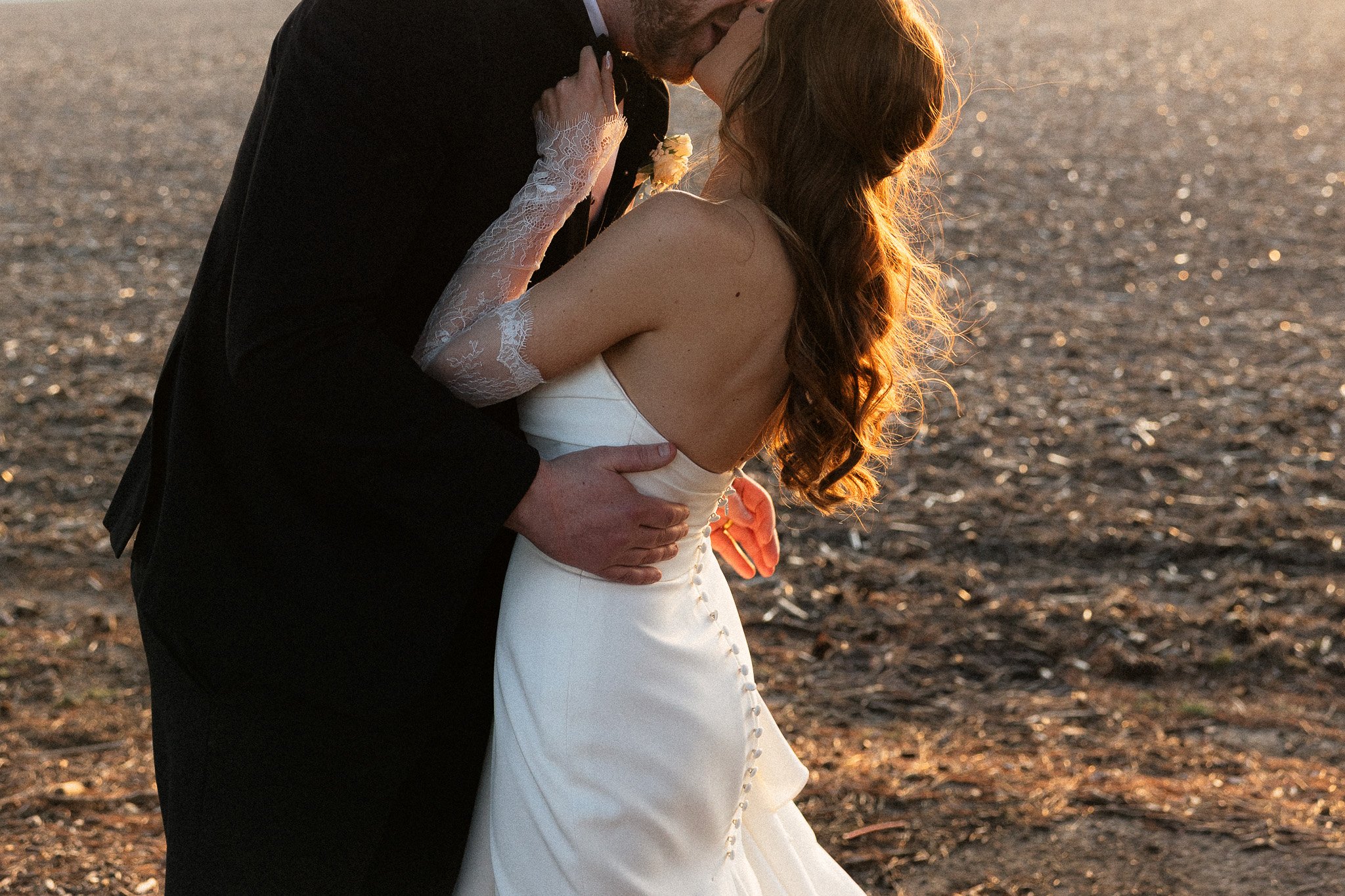 Bride and groom holding each other and kissing at golden hour in a field.