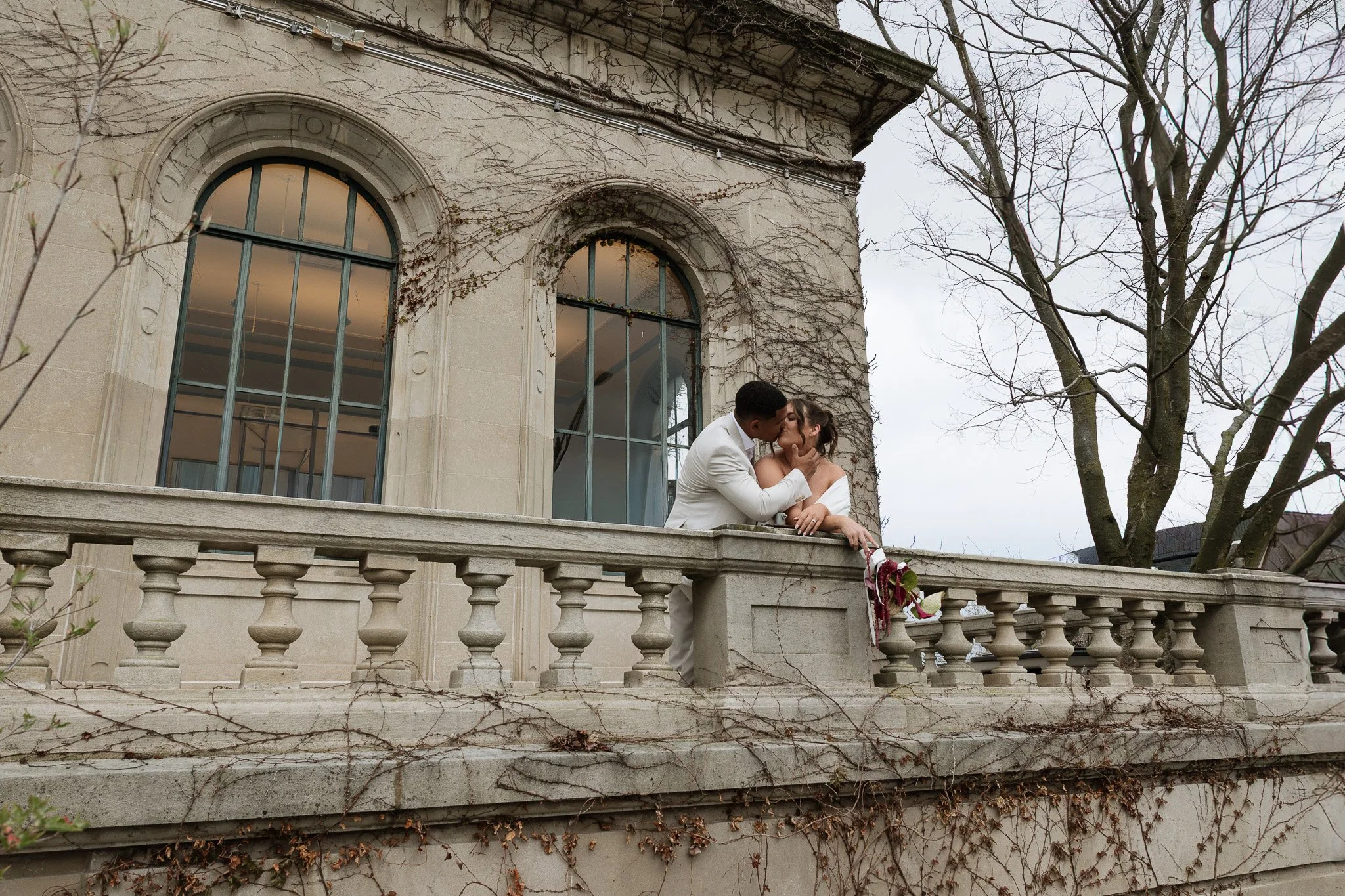 A bride and groom holding one another and kissing on the balcony of Urbana Library