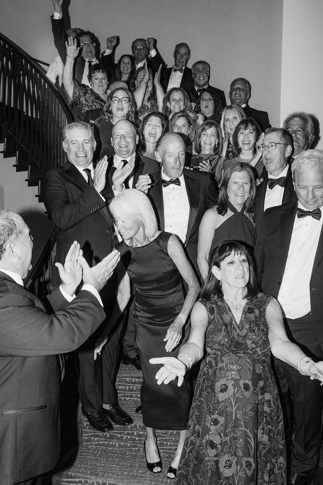 A large group of people dressed in formal attire, gathered on a staircase, celebrating at a social event or party.