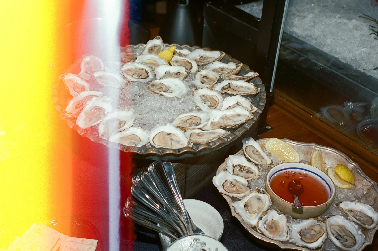 Plate of fresh oysters on ice with lemon wedges and a bowl of cocktail sauce.