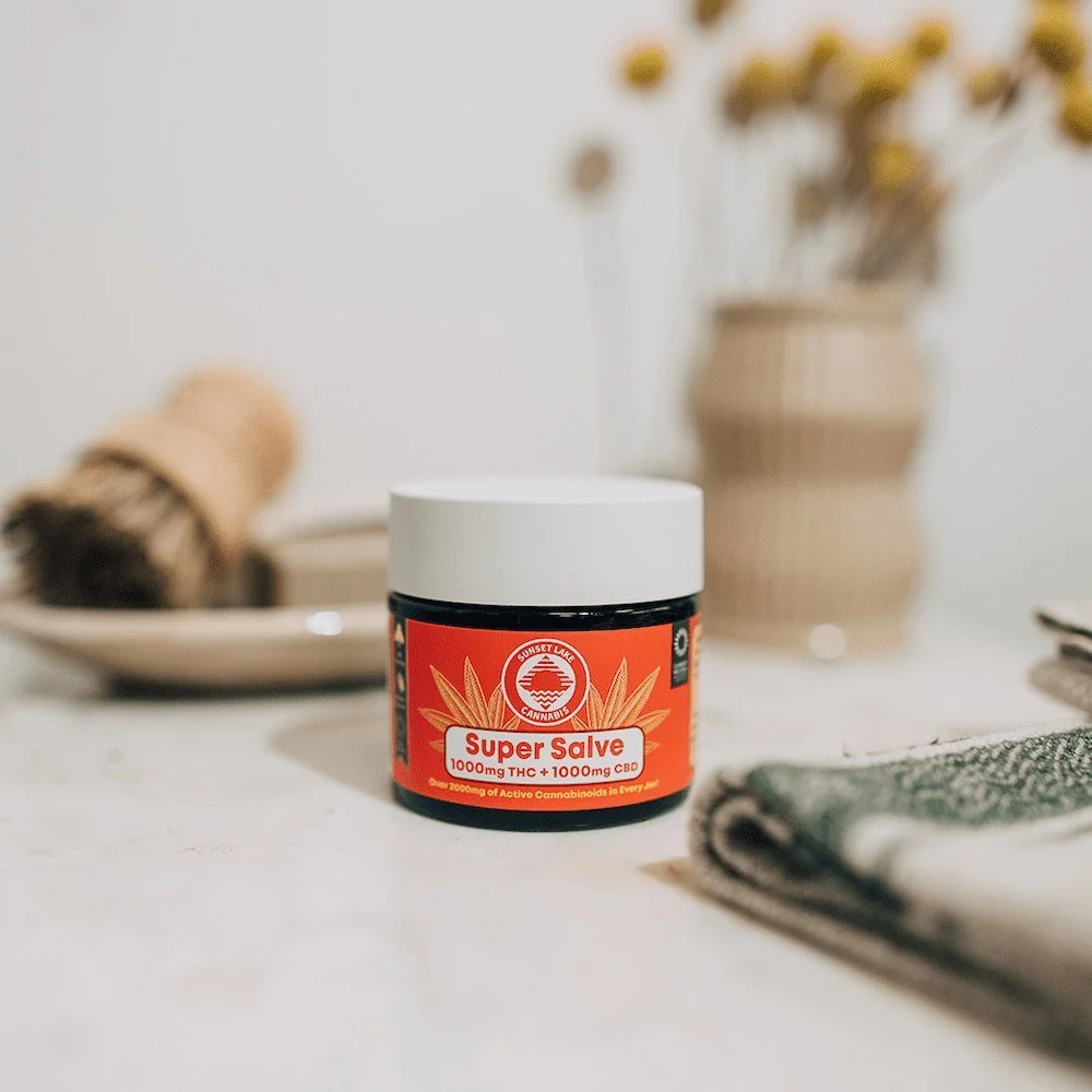 Jar of Sunset Lake Cannabis Super Salve THC topical on a bathroom sink counter next to shaving brush and hand towel