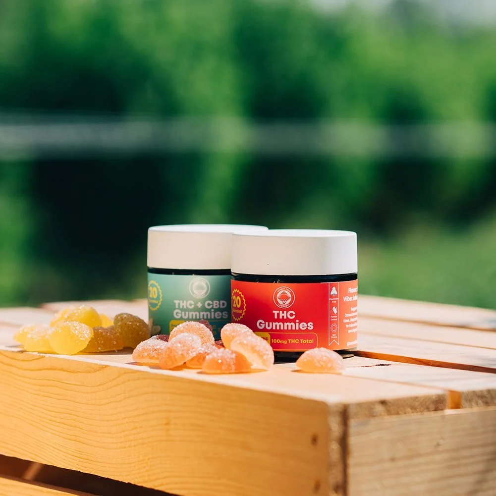 Jars of Sunset Lake Cannabis THC gummies on a wooden crate in front of out-of-focus cannabis plants.